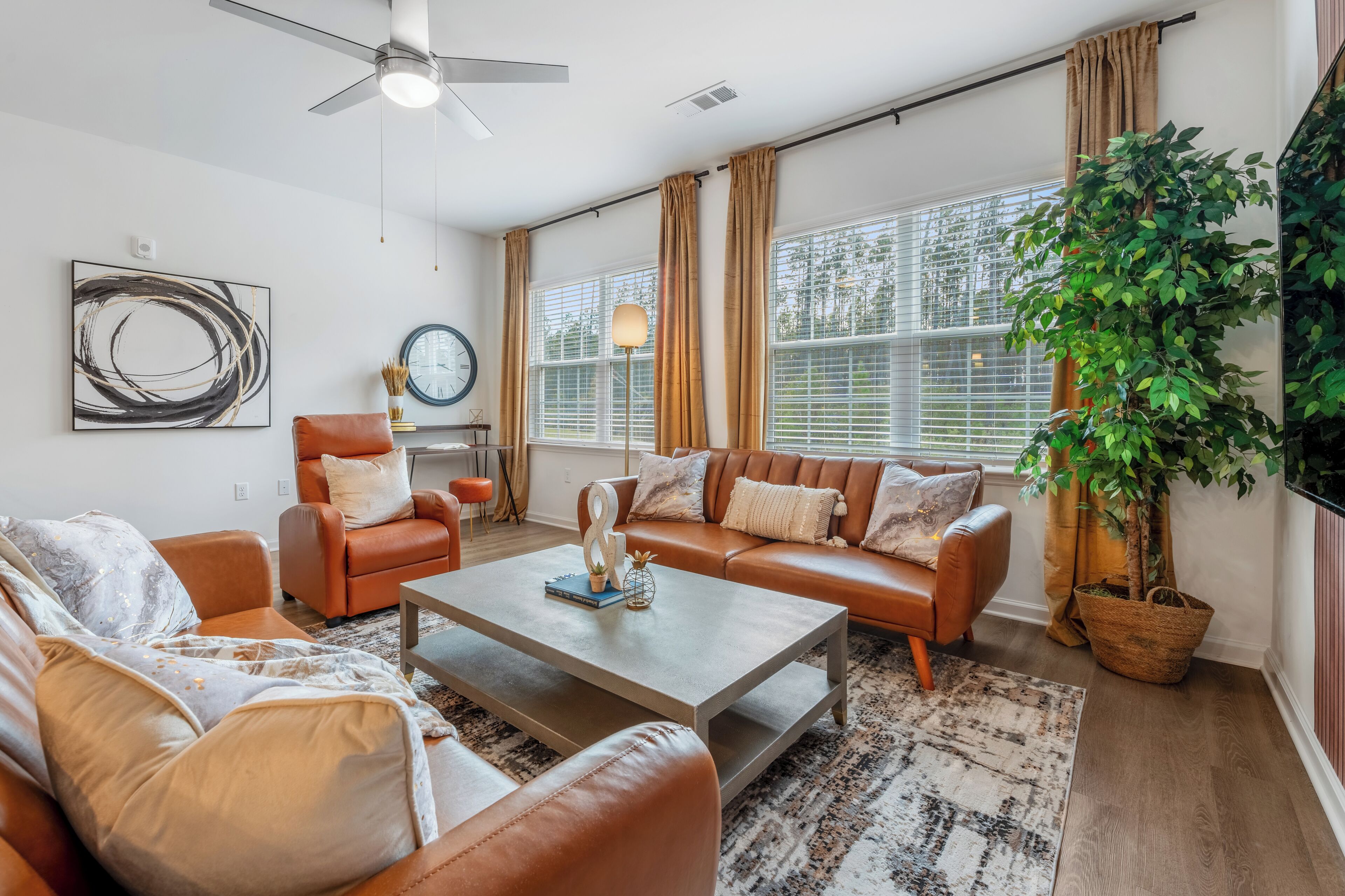 A living room with a sofa set, a coffee table, a chair, a clock, a plant, and large windows with curtains.