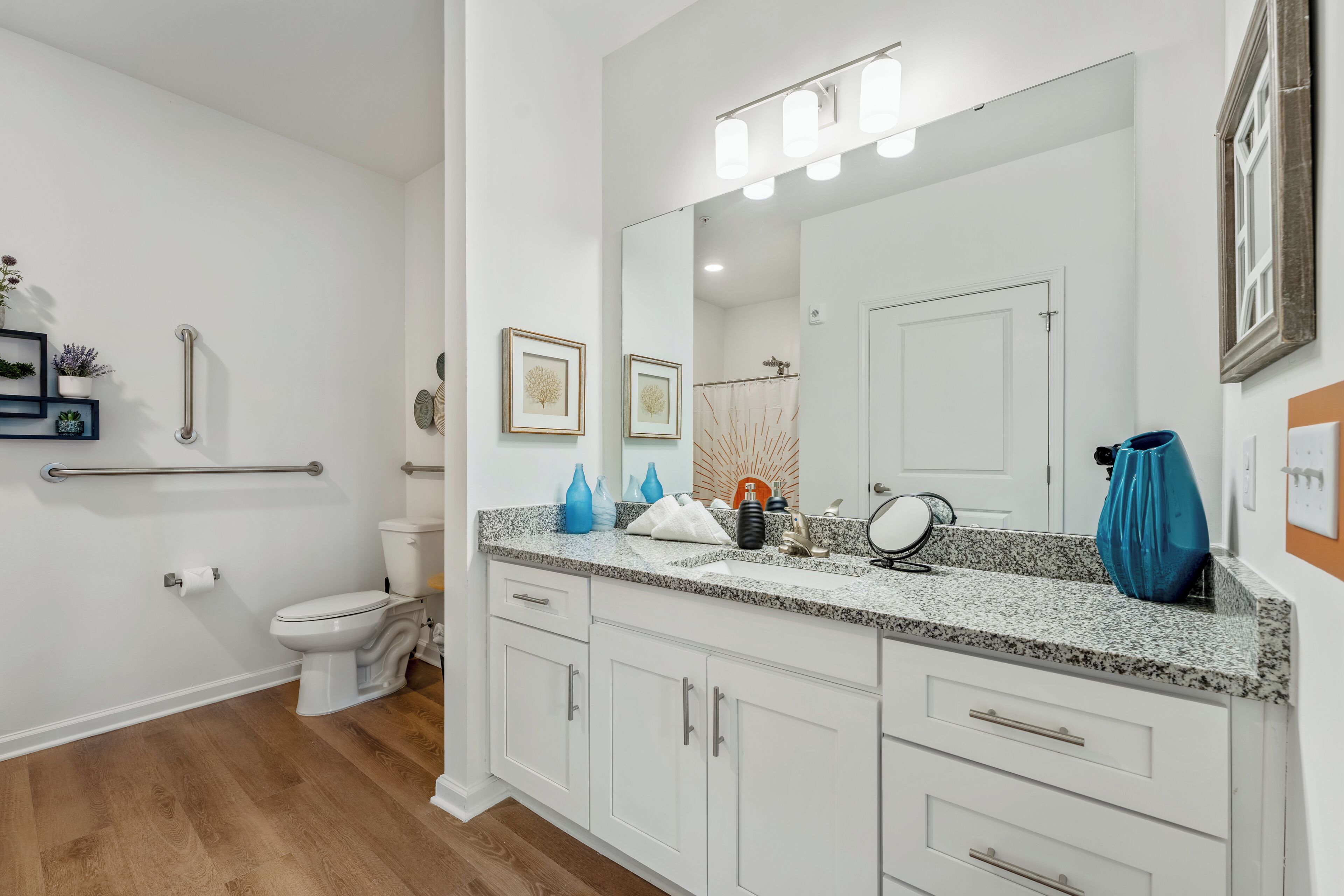 Un baño moderno con un inodoro blanco, un lavabo con encimera de granito y un espejo grande con luces.