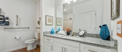 Un baño moderno con un inodoro blanco, un lavabo con encimera de granito y un espejo grande con luces.