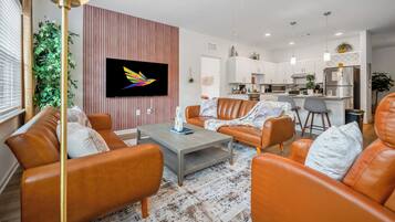 A modern living room with orange leather sofas, a coffee table, and a TV mounted on a wall.