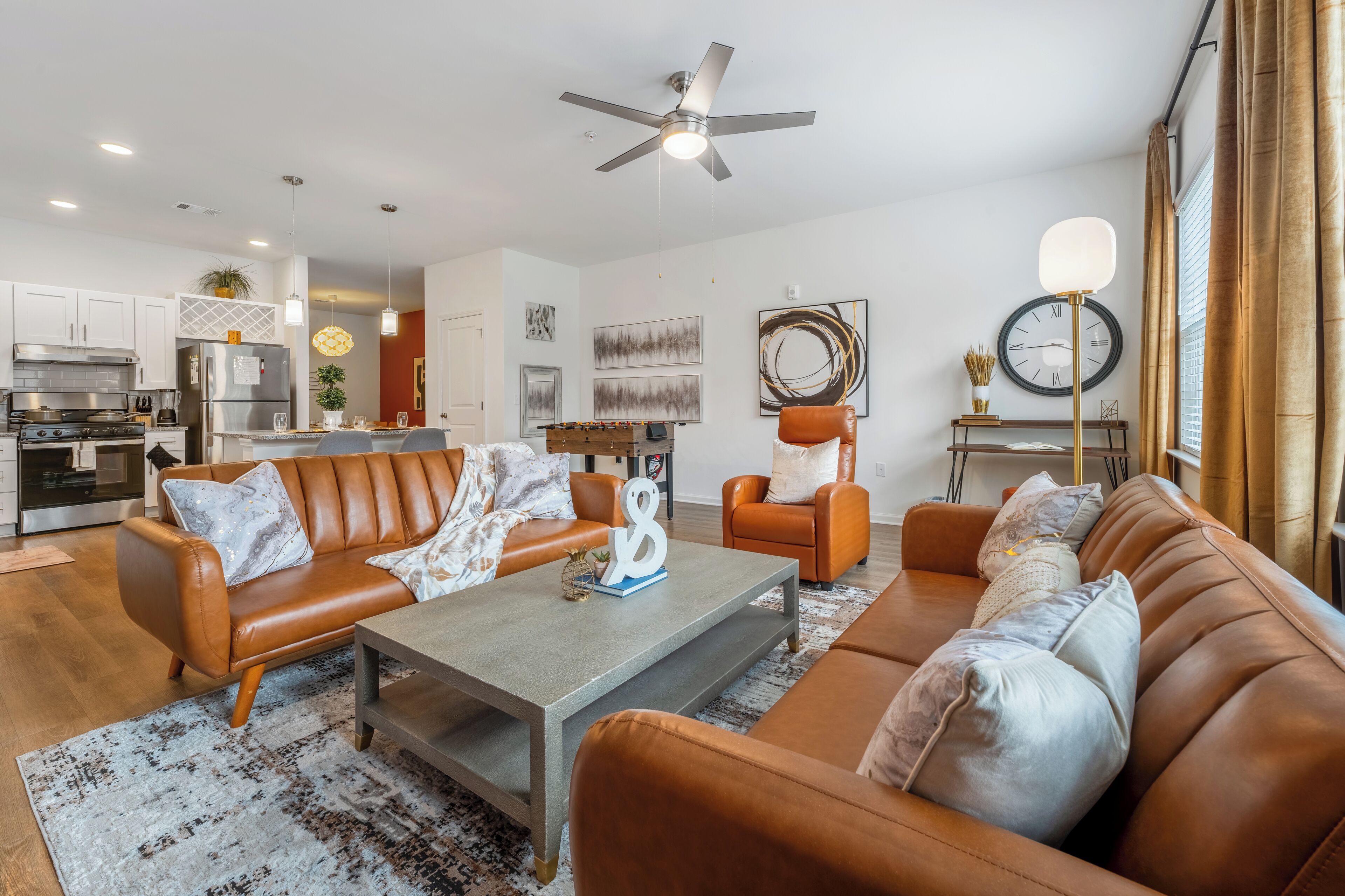 A modern living room with leather sofas, a coffee table, and a dining area with a foosball table.