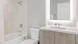 A bathroom with a bathtub, toilet, and vanity with a mirror. - Shaw #501 | 2BR | Balcony, City Views & Garage (washington)