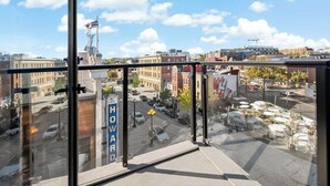 A view from a high-rise building with a clear sky, a street with parked cars, and a flagpole with an American flag. - Shaw #501 | 2BR | Balcony, City Views & Garage (washington)