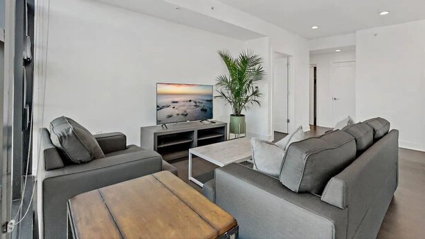 A modern living room with a grey sofa, a coffee table, a TV, and a plant. - Shaw #501 | 2BR | Balcony, City Views & Garage (washington)