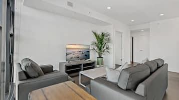 Ein stilvolles Wohnzimmer mit grauem Sofa, Couchtisch, Fernseher und einer Pflanze.