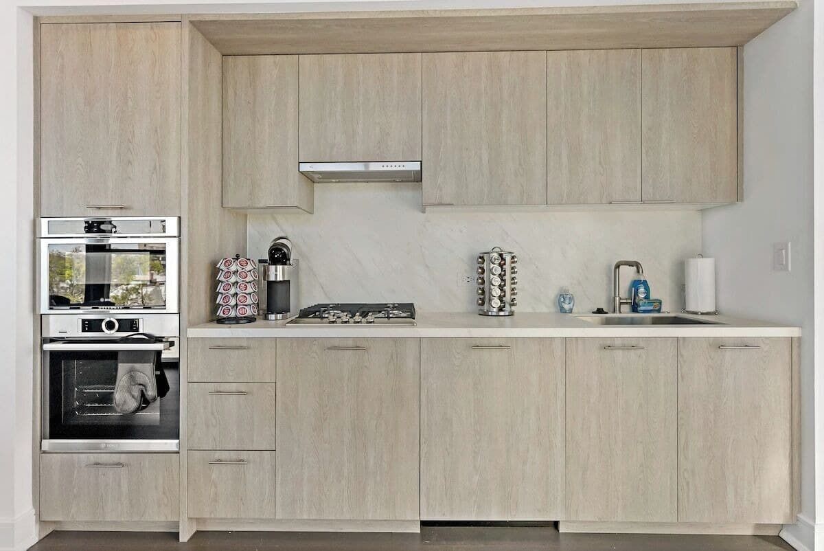 Eine moderne Küche mit hellen Holzschränken, einem Einbauofen, einer Kaffeemaschine und einem Spülbecken mit Armatur.
