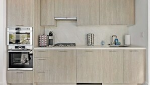 A modern kitchen with light wood cabinetry, a built-in oven, a coffee machine, and a sink with a faucet. - Shaw #501 | 2BR | Balcony, City Views & Garage (washington)