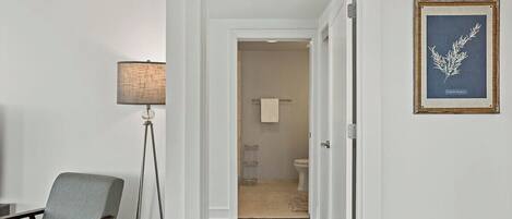 Un pasillo que conduce a un baño con un inodoro, un perchero para toallas e ilustración botánica enmarcada en la pared.