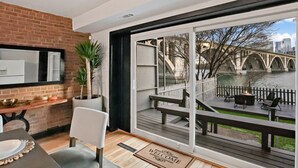 A modern interior with a dining area, a large sliding glass door leading to an outdoor deck with a view of a bridge and river. - Georgetown 4BR Waterfront Townhome | Potomac Views & Parking (Washington)