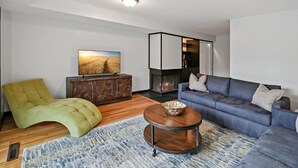 A modern living room with a sofa, a green armchair, a wooden coffee table, a fireplace, and a television on a cabinet. - Georgetown 4BR Waterfront Townhome | Potomac Views & Parking (Washington)