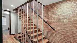A staircase with wooden steps and metal railings, leading to a room with a brick wall and a window. - Georgetown 4BR Waterfront Townhome | Potomac Views & Parking (Washington)