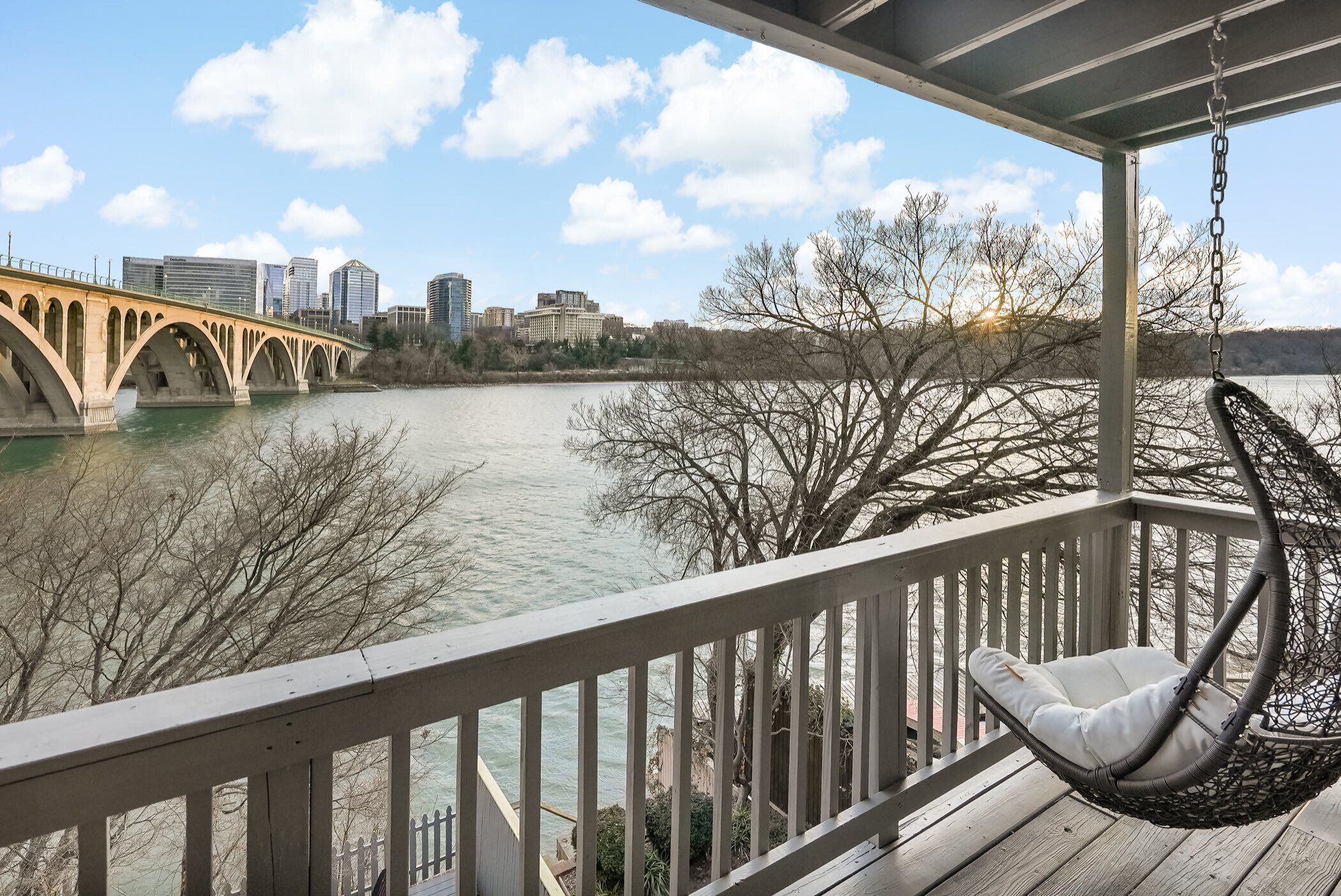 Une terrasse en bois avec un fauteuil suspendu donnant sur une rivière et un pont.