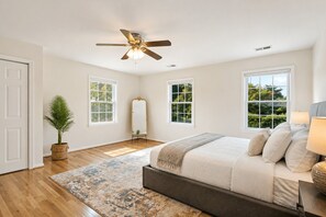 A bedroom with a bed, a ceiling fan, a potted plant, and a large window.