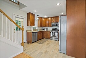 A kitchen with wooden cabinets, stainless steel appliances, and a wooden staircase.