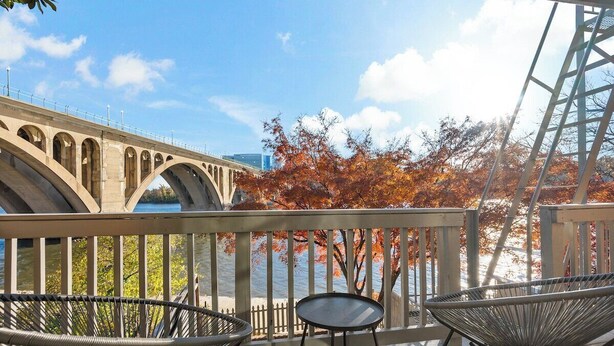 Ein Balkon mit Korbstühlen und einem Tisch mit Blick auf eine Brücke und Herbstlaub.