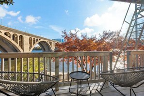 Ein Balkon mit Korbstühlen und einem Tisch mit Blick auf eine Brücke und Herbstlaub.