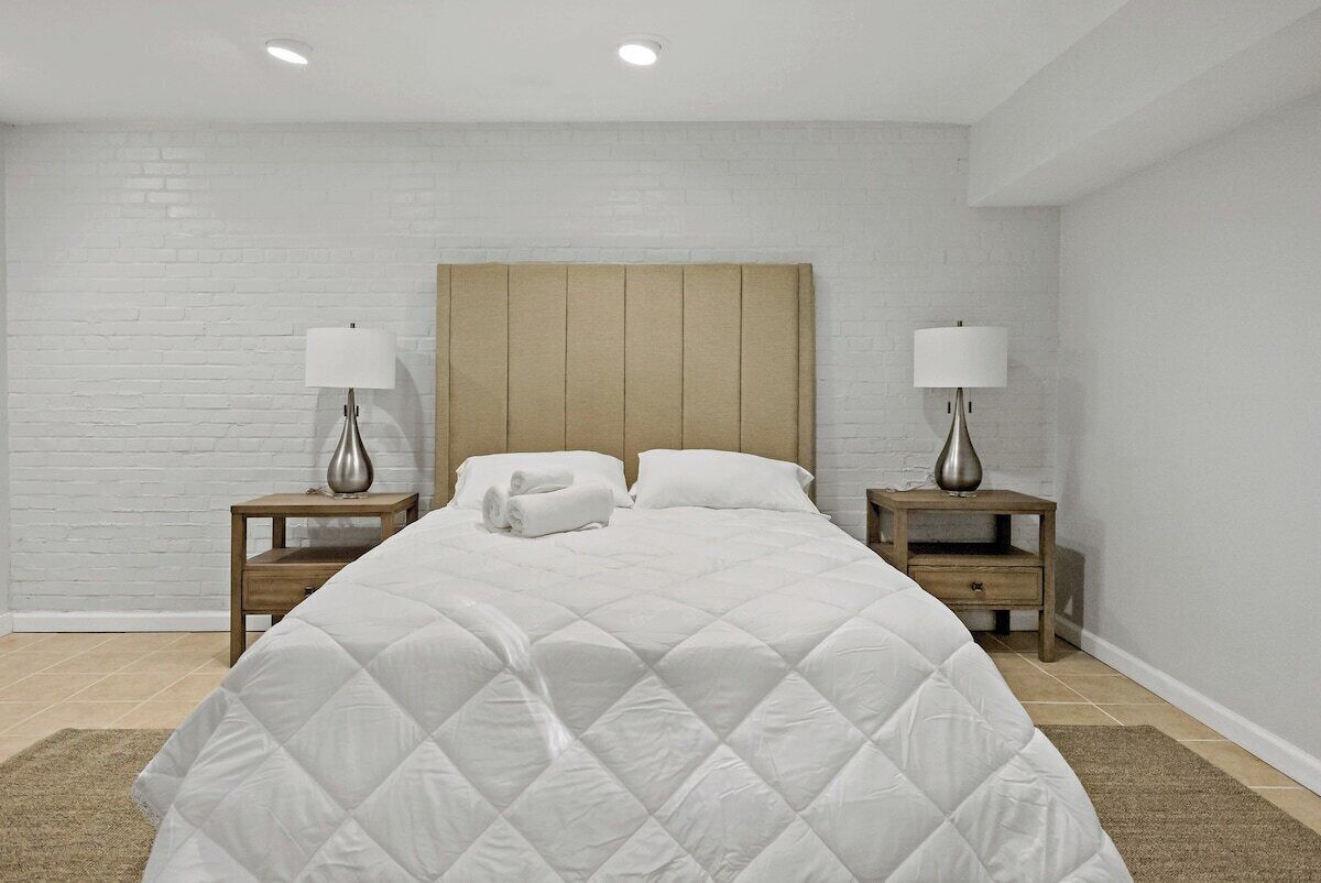 A neatly made bed with a quilted white duvet, two bedside tables with lamps, and a wooden headboard.