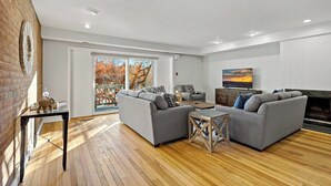 Ein modernes Wohnzimmer mit Kamin, zwei grauen Sofas, einem Couchtisch und einem großen Fenster mit Blick auf Bäume.