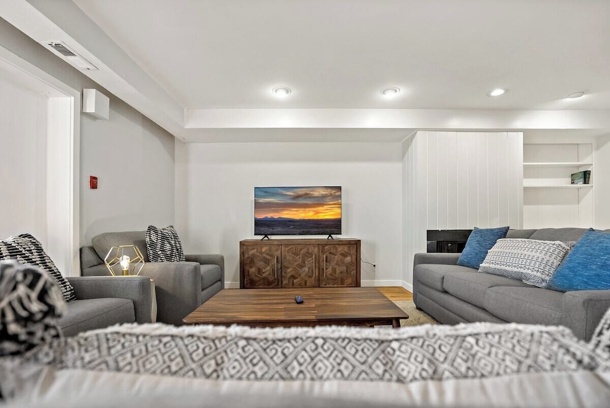 A modern living room with two grey sofas, a wooden coffee table, and a painting of a sunset.