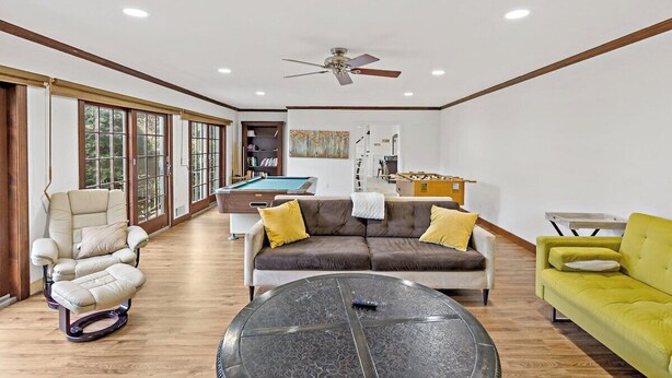 Amplia sala de estar con mesa de billar, un sofá, un sillón amarillo y un ventilador de techo.