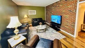 Ein Wohnzimmer mit Backsteinwand, einem Fernseher, Ledersofas, einem Couchtisch und einer Lampe.