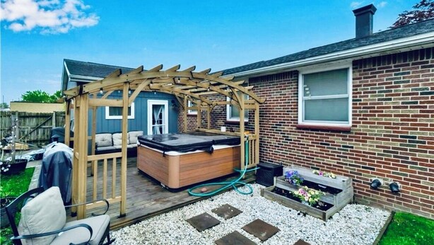 Ein Garten mit einer Holz-Pergola, einem Whirlpool und einem Ziegelhaus.
