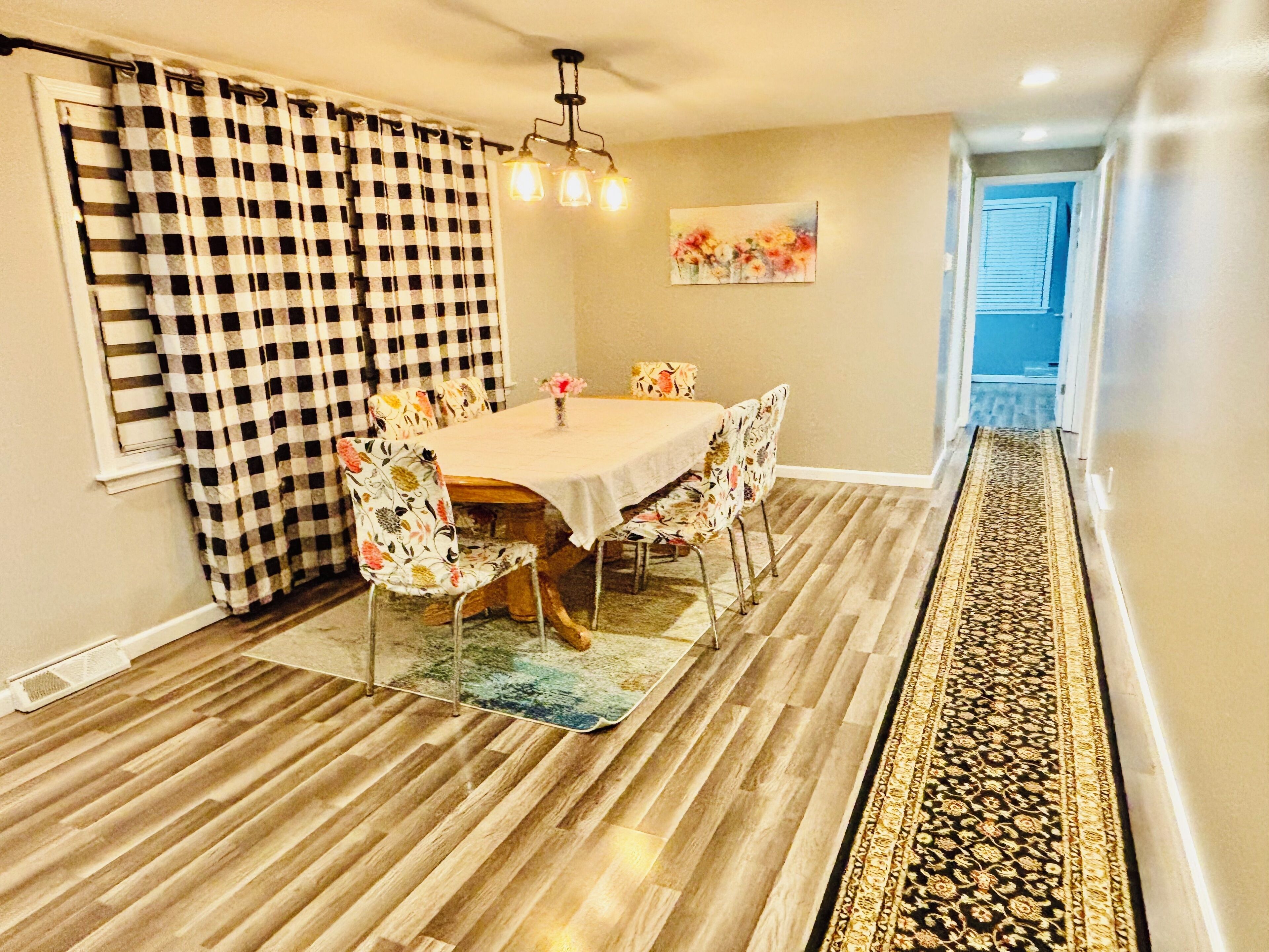 A dining area with a checkered curtain, floral chairs, a wooden table, and a patterned rug.