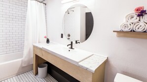 Een moderne badkamer met een wit wastafelblad, een houten kastje, een ronde spiegel en een handdoekrek met opgerolde handdoeken.