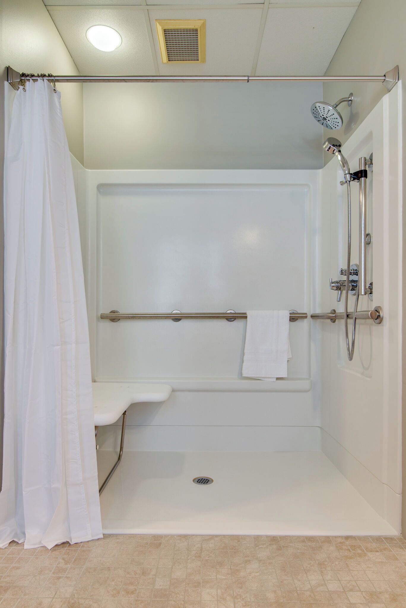 Une cabine de douche blanche, dotée d’un pommeau de douche à main, d’un porte-serviettes et d’un rideau de douche.