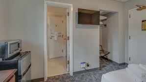 A hotel room with a kitchenette, a TV mounted on the wall, a bed, and a door leading to a bathroom. - Charming Suite in Music Row! (Nashville)