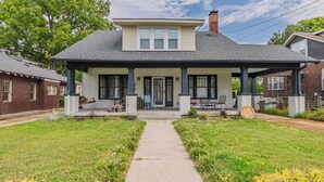 A two-story house with a covered porch, a front yard with a pathway, and a brick chimney.