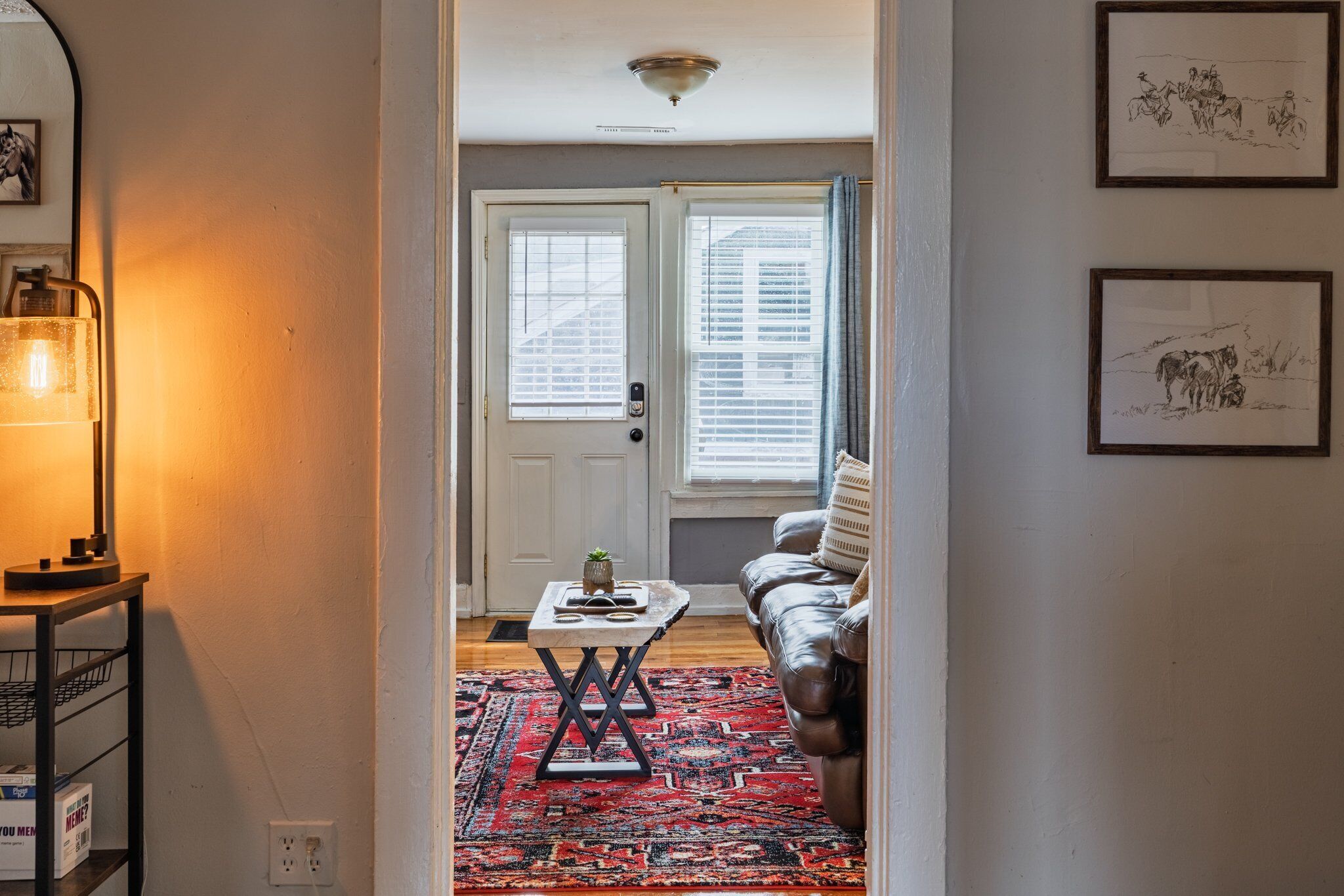 A hallway leading to a living room with a red patterned rug, a brown leather sofa, and a door with a window.
