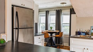 A modern kitchen with a stainless steel refrigerator, white cabinets, a dark countertop, and a dining area with two chairs and a table.