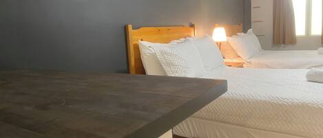 Une chambre d’hôtel avec deux lits, une tête de lit en bois, du linge de lit blanc, un bureau et une chaise.