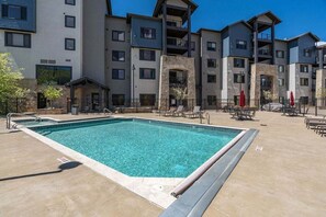 A swimming pool with lounge chairs, a covered seating area, and a multi-story building with balconies.