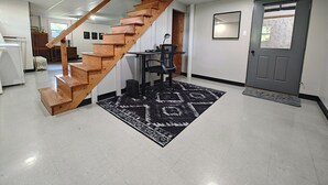 Um interior moderno com uma escada de madeira que leva a um segundo andar, um tapete estampado em preto e branco, uma porta cinza e uma pequena mesa com uma cadeira.