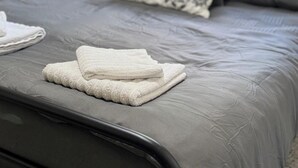 Un lit bien fait, avec une couette grise, un oreiller à motifs et des serviettes blanches pliées.