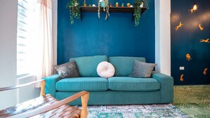 A teal sofa with cushions, a patterned rug, a wooden bench, and a wall with hanging plants and animal silhouettes.