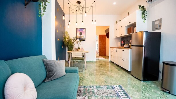 A modern kitchen with a refrigerator, a dining area with a table and chairs, and a living room with a sofa.