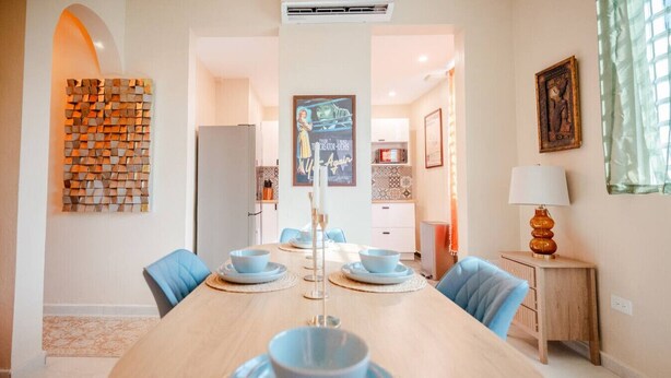 A dining area with a long wooden table set for four, blue chairs, and a decorative wall piece. - Casa Lotus「UNIT 2「Tembleque」 (San Juan)