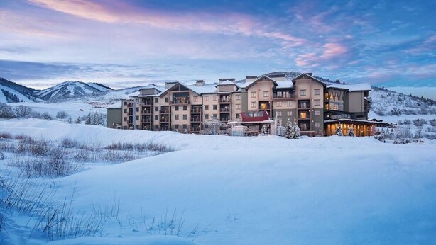 A multi-story hotel with a snow-covered landscape and mountains in the background.