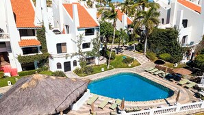 Un resort con piscina, edificios blancos con techos rojos y palmeras.