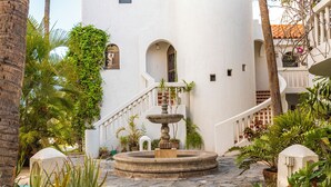 Un patio con una fuente central, rodeado de plantas en macetas y palmeras.