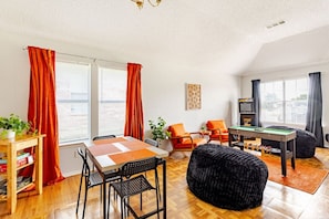A living room with a wooden table, orange chairs, a black ottoman, and a pool table. - 3BR Large Family Oasis | PS5, Arcades + Fast WiFi (Arlington)