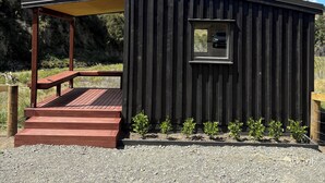 Une petite cabane en bois avec une fenêtre, une terrasse en bois et un espace salon couvert.