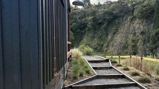 Un bâtiment en bois avec un escalier métallique menant à une zone recouverte de gravier.
