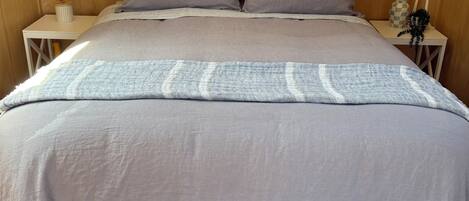 Una cama con un edredón a rayas gris y blanco, un cabecero de madera y dos mesitas de noche con velas y un florero.