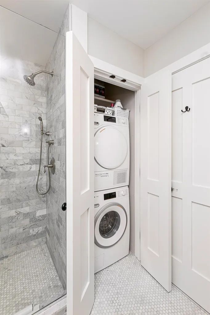 A compact bathroom with a shower, a stacked washer and dryer, and white doors.