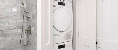 A compact bathroom with a shower, a stacked washer and dryer, and white doors.