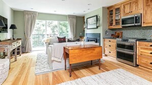 Un salon spacieux doté d’une grande fenêtre, d’une cheminée, de meubles en bois et d’un coin cuisine équipé d’appareils électroménagers modernes.